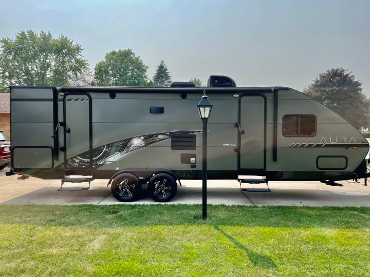 A large, modern grey travel trailer with graphic decals, parked on a driveway, ready for RV rental.. Travel Lite Aura 2019