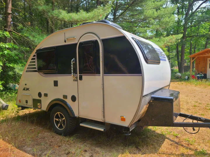 Compact cream teardrop RV rental, perfect for camping in a serene woodland setting.. Xtreme Outdoors Little Guy 2019