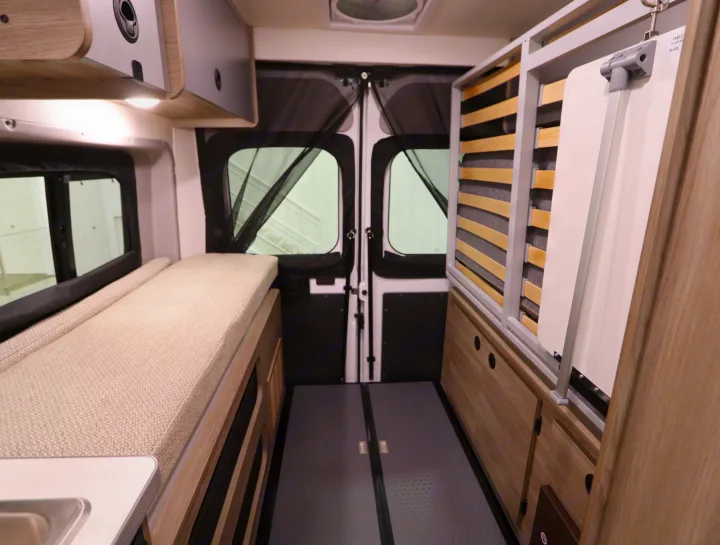 Inside a modern RV rental: a compact interior with bed, overhead storage, rear doors with mesh, and a multi-functional table/bed setup.. Winnebago Solis 2021