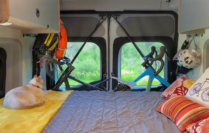 Inside an RV rental: a cozy bed with a cat, clever bike storage, & hanging gear. Ideal for adventure travel.. Winnebago Solis 2021