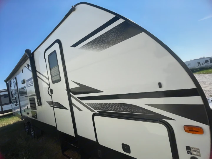 White and black RV rental, a travel trailer with geometric patterns and stripes, parked outside under a clear blue sky.. Dutchmen Coleman Light 2022