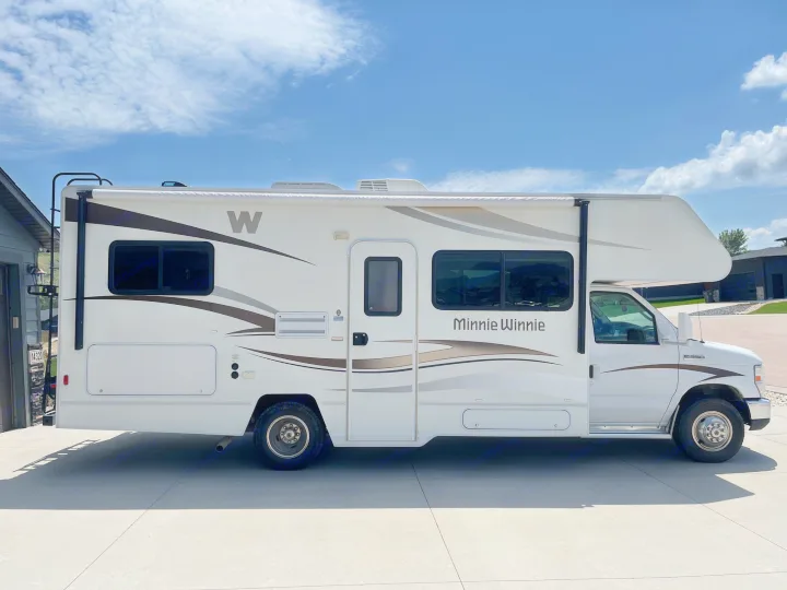 White Class C RV rental, a Minnie Winnie motorhome, parked on a driveway under a blue sky.. Winnebago Minnie Winnie 2014
