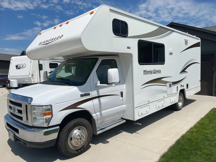 This white Winnebago Minnie Winnie RV rental, a Class C motorhome, is parked on a sunny concrete driveway.. Winnebago Minnie Winnie 2014