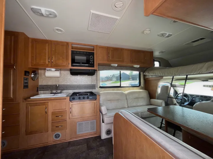 Spacious RV rental interior featuring a full kitchen, dining area, comfortable sofa, and over-cab bunk bed.. Winnebago Minnie Winnie 2014