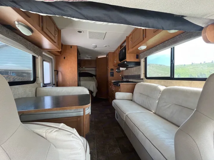 Bright, spacious RV rental interior: view of the kitchen, dining booth, and sofa seating area with landscape views.. Winnebago Minnie Winnie 2014