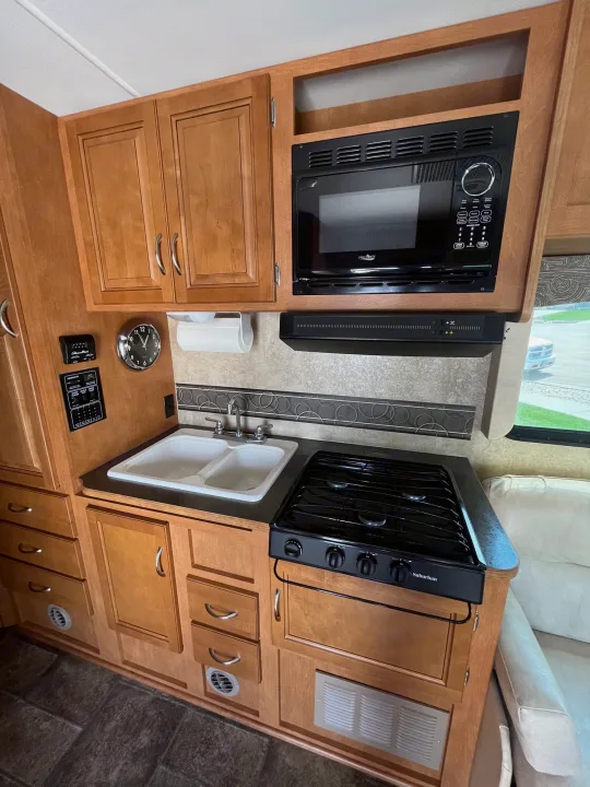 Explore the well-equipped kitchen in this RV rental, featuring a dual sink, stove, microwave, and wood cabinetry.. Winnebago Minnie Winnie 2014