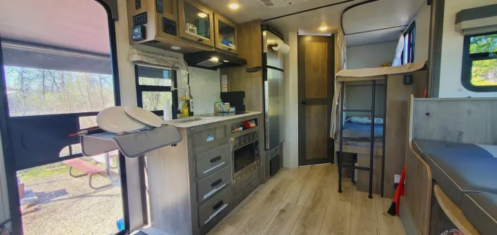 RV rental interior: kitchen with sink/stove, microwave, fridge, bunk beds, and outdoor view. Ideal for travel.. Forest River Surveyor Legend 2022