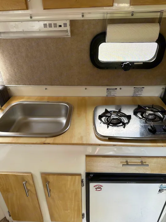 Inside an RV rental, a compact kitchen with a stainless steel sink, two-burner stove, and small Dometic refrigerator.. Scamp Scamp Trailer 2010