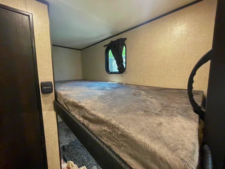 RV rental interior: A comfy bunk bed with a soft gray blanket, window, and thermostat on the wall. Ideal for travel.. Jayco Jay Flight 2022