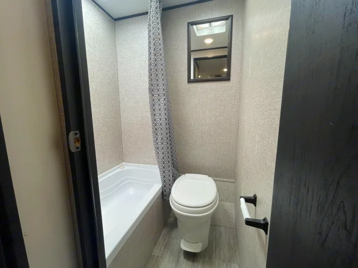 Compact RV rental bathroom with a toilet, tub, modern shower curtain, and mirror. Perfect for your travels.. Jayco Jay Flight 2022