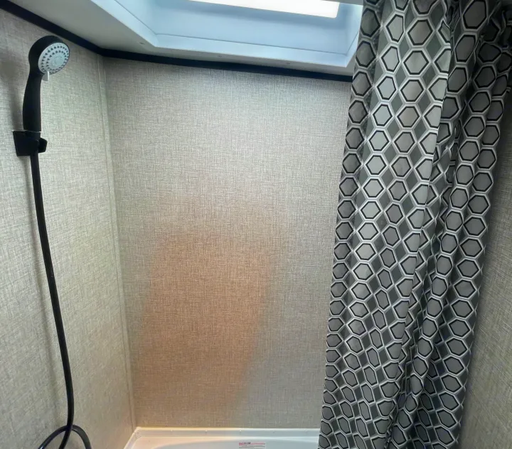 Inside an RV rental, a compact shower stall features a handheld showerhead, textured walls, and a grey geometric curtain.. Jayco Jay Flight 2022