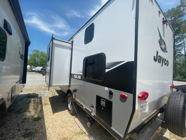 This Jayco SLX travel trailer, perfect for rv rental, shows an open slide-out, rear spare tire, and utility connections.. Jayco Jay Flight 2022