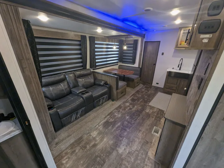 Spacious RV rental interior with black recliners, a dinette, kitchen area, wood flooring, and blue accent lighting.. Forest River Cherokee Wolf Pack Toy Hauler 2022