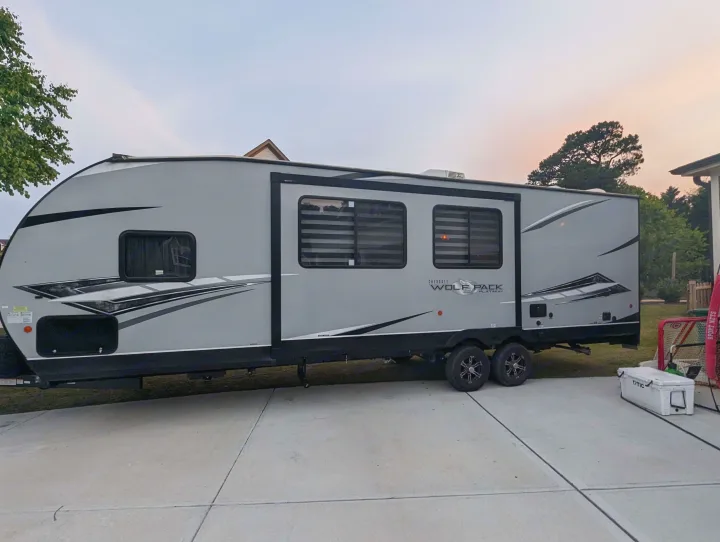 A large grey Cherokee Wolf Pack travel trailer, a great option for RV rental, is parked on a paved driveway.. Forest River Cherokee Wolf Pack Toy Hauler 2022
