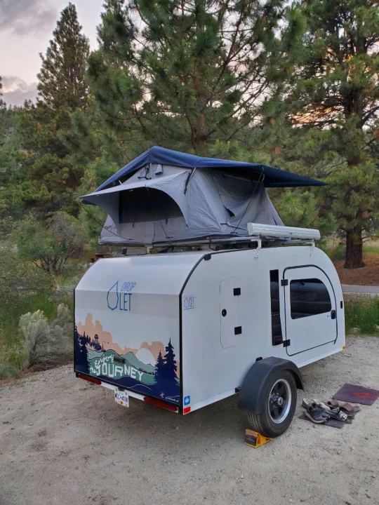 An RV rental teardrop trailer with a rooftop tent set up in a pine forest, perfect for camping adventures.. droplet XL 2026
