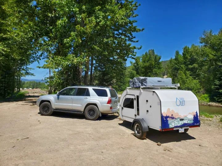 Silver SUV towing a white Droplet teardrop RV rental, packed for an outdoor journey by the river.. droplet XL 2026