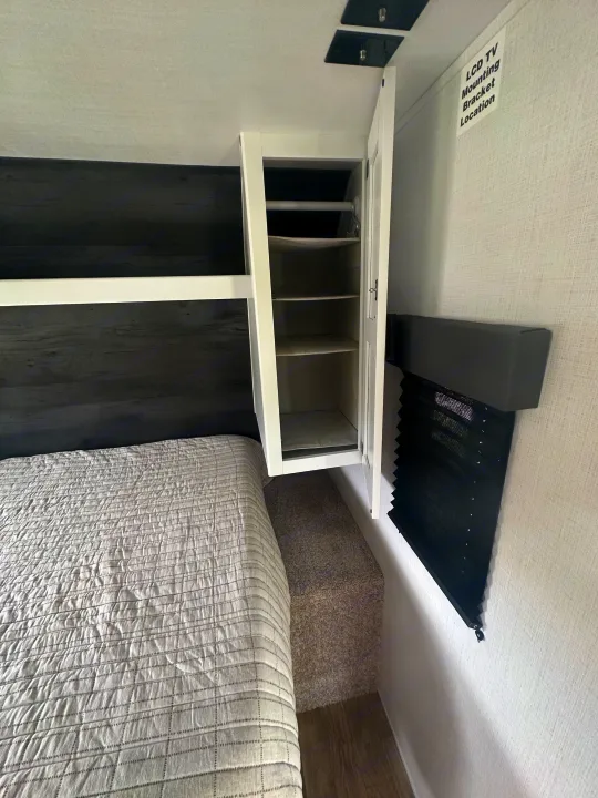 RV rental bedroom with a cozy bed, open storage cabinet, and TV mounting location, optimized for compact living.. Keystone RV Hideout 2023