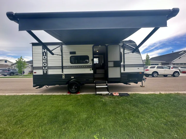 This RV rental, a travel trailer with its awning extended, is parked on a street with its door open.. Keystone RV Hideout 2023