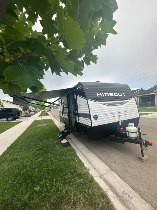 Black and white Hideout RV rental with an extended awning, parked on a residential street. It's ready for adventure!. Keystone RV Hideout 2023