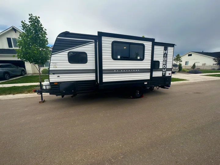 An RV rental travel trailer with extended slide, parked on a suburban street under an overcast sky.. Keystone RV Hideout 2023
