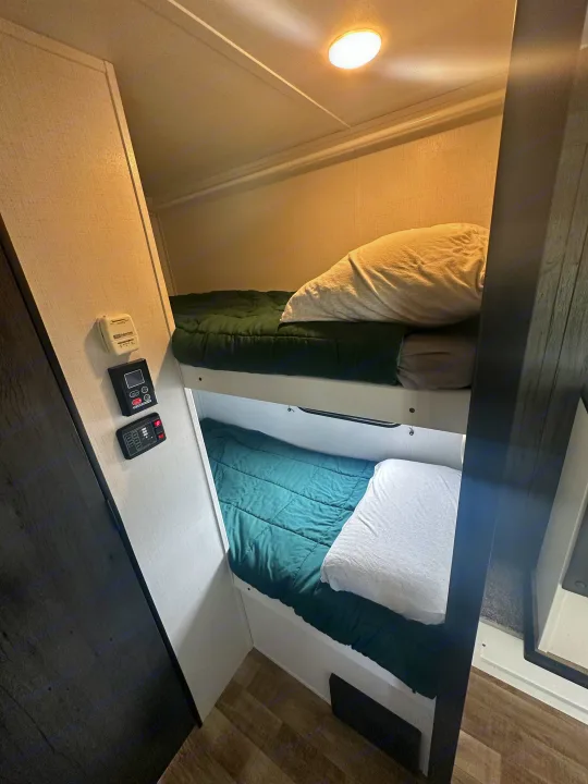 Cozy bunk beds within an RV rental, featuring a thermostat and control panel on the wall for a comfortable stay.. Keystone RV Hideout 2023