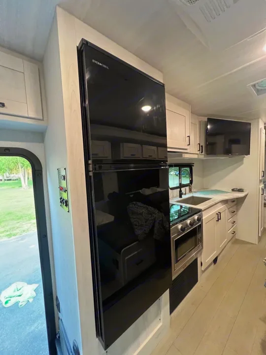 Explore this RV rental's modern kitchen: black fridge, oven, sink, and light cabinets for comfortable travel.. EAST TO WEST ENTRADA  2600DS 2023