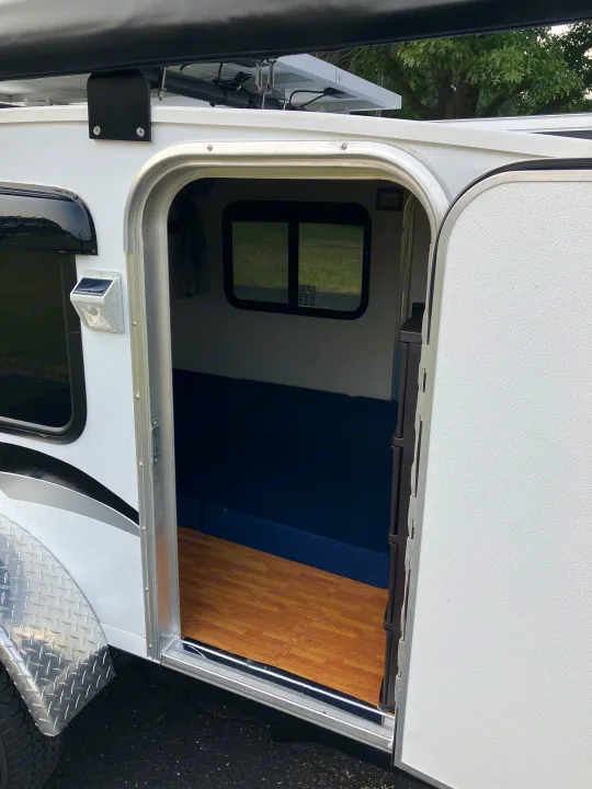 Compact white travel trailer RV rental interior with blue mattress, wood floor, solar light. Awning & solar panel visible.. Runaway Campers Rangerunner 2021