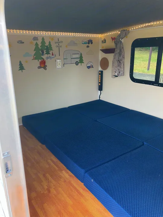 RV rental interior: blue fold-out mattresses, wood-look floor, charming camping wall decals, and warm string lights.. Runaway Campers Rangerunner 2021