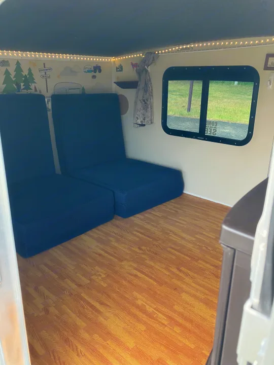 Versatile RV rental interior with convertible blue seating, wood flooring, and charming campsite wall decor.. Runaway Campers Rangerunner 2021