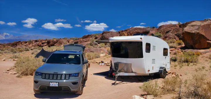 Jeep and white travel trailer RV rental parked at a desert campsite, with rocky hills and distant snow-capped mountains.. InTech RV Sol Horizon 2020
