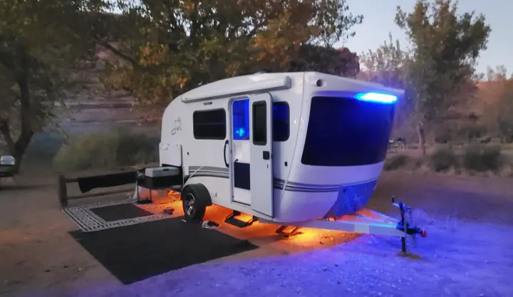 A modern RV rental travel trailer is brightly lit with blue and orange LED lights at a tranquil nighttime campsite.. InTech RV Sol Horizon 2020