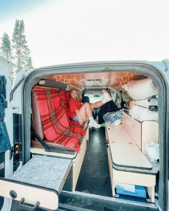Smiling woman relaxing in a well-equipped RV rental, ready for a fun camping and road trip adventure.. Dodge Promaster City 2018