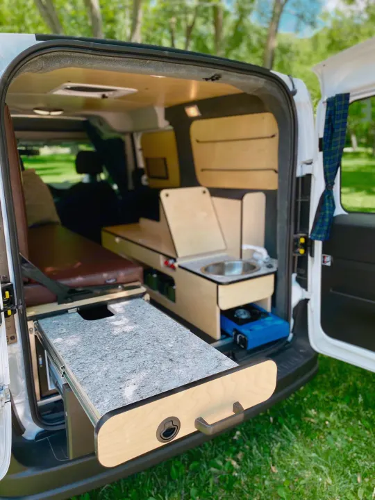 RV rental: Camper van interior with pull-out kitchen, sink, stove, and bed area.. Dodge Promaster City 2018