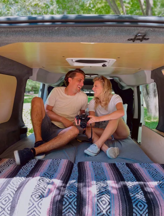 Cozy RV rental: A laughing couple relaxes inside their converted camper van, camera in hand.. Dodge Promaster City 2018