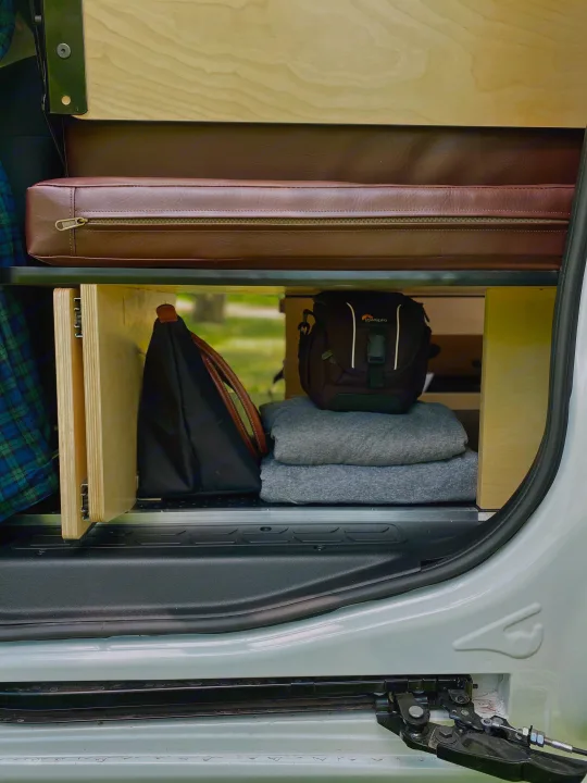 Organized RV rental storage featuring a brown cushion, wooden shelving, a camera bag, and cozy blankets.. Dodge Promaster City 2018