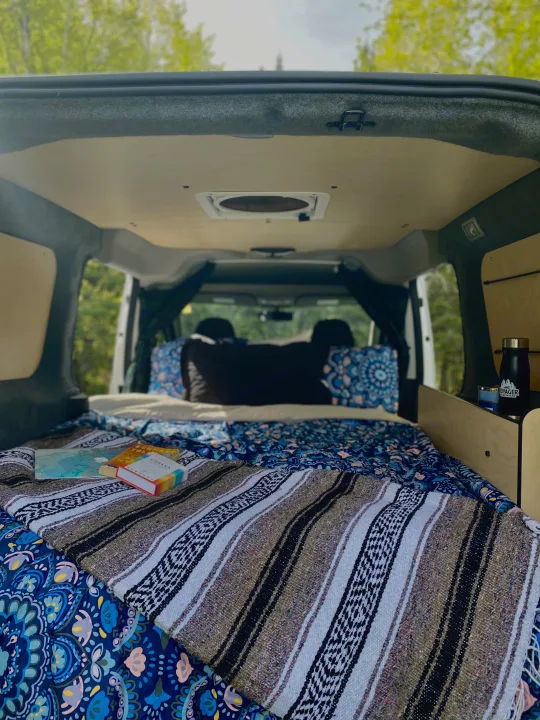 Cozy camper van interior: a perfect RV rental setup for relaxing road trips, complete with a bed, books, and nature views.. Dodge Promaster City 2020