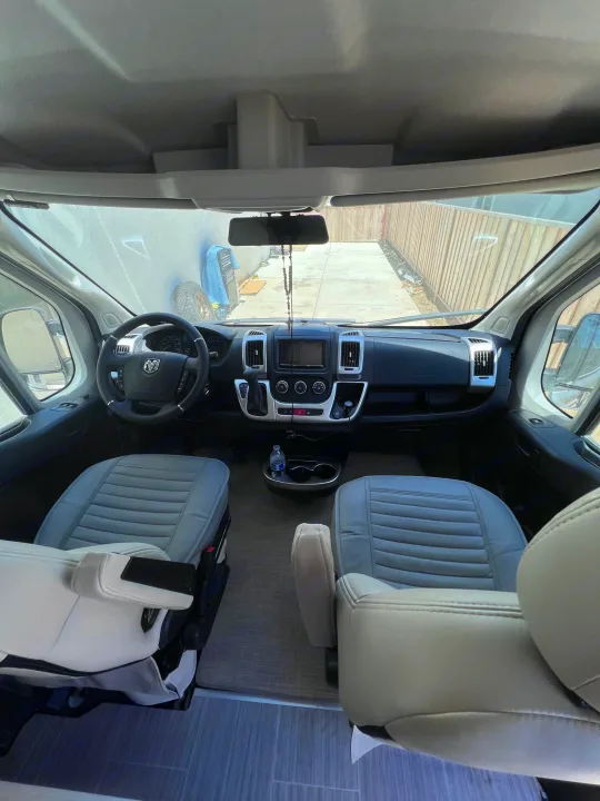 Inside this RV rental: a bright, spacious camper van cockpit with driver/passenger seats & dashboard visible.. Thor Tellaro 2021