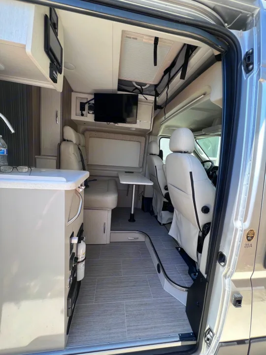 Inside a modern **rv rental**: light gray interior with kitchen, dining table, and swivel front seats. Ready for your trip!. Thor Tellaro 2021