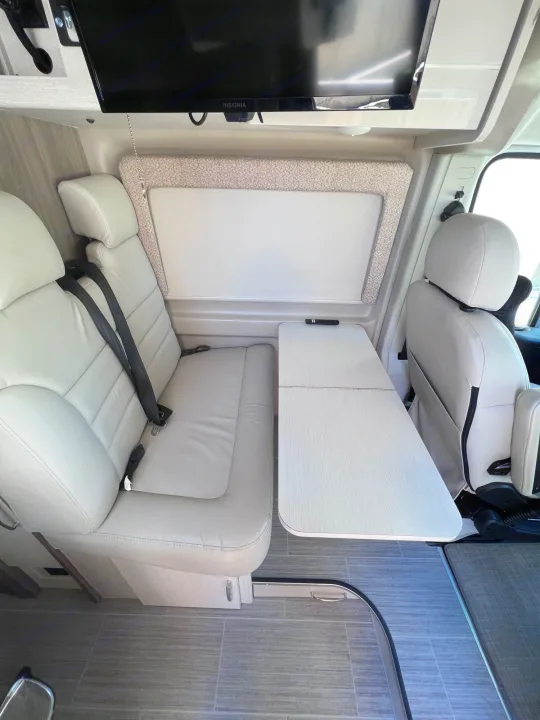 Modern RV rental interior with light seating, fold-out table, and TV, offering a compact dining/lounge area.. Thor Tellaro 2021