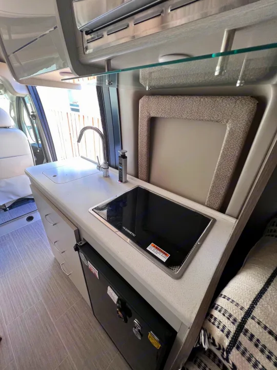 Compact RV rental kitchen interior: features a Dometic induction cooktop, sink, pop-up outlet, and mini-fridge.. Thor Tellaro 2021