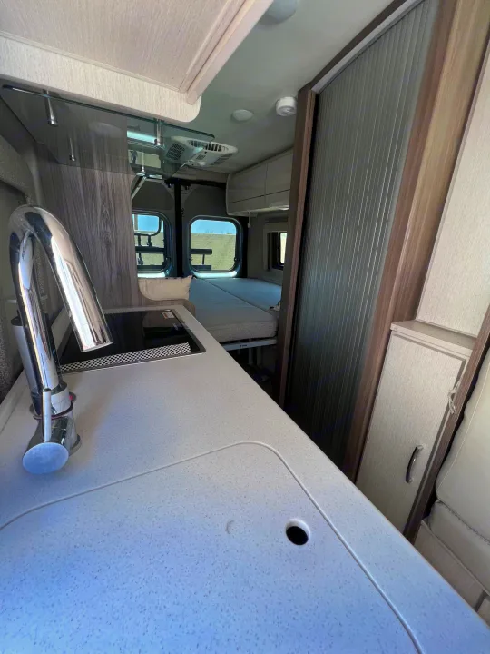 RV rental interior: modern kitchen with sink & stovetop, leading to a compact bedroom with windows. Ideal for travel.. Thor Tellaro 2021