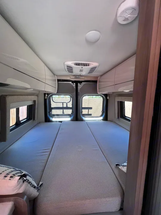 Spacious RV rental interior featuring a large bed, overhead storage, AC unit, and rear windows, ready for travel.. Thor Tellaro 2021