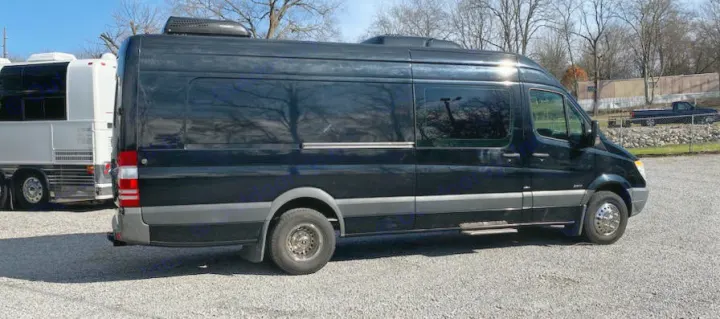 Black Mercedes-Benz Sprinter van, often used for RV rental, parked on a gravel lot next to other large vehicles.. Mercedes-Benz Sprinter 2012