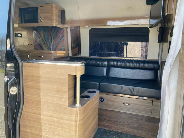 Spacious RV rental interior with black leather lounge seating, wooden cabinetry, and modern kitchen amenities.. Mercedes-Benz Sprinter 2012