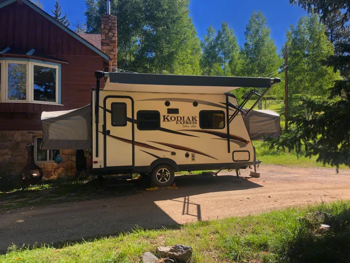 Kodiak Express RV rental parked at a rustic cabin, with tent-like pop-outs extended for camping and an awning deployed.. Dutchmen Kodiak Express 2017