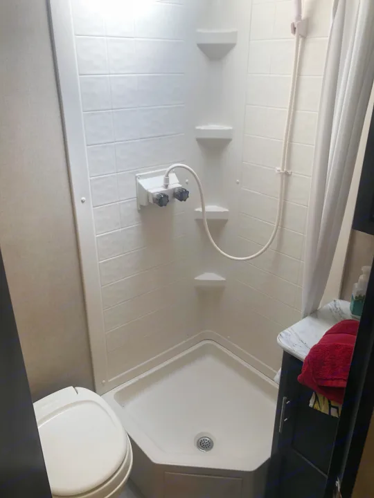 A compact RV rental bathroom featuring a white shower with a flexible showerhead, and a toilet visible on the right.. Dutchmen Kodiak Express 2017