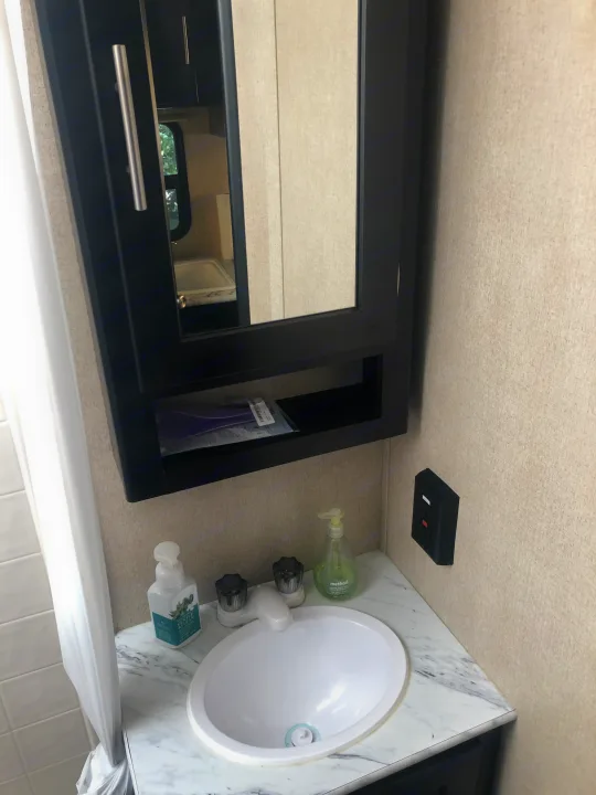 Compact RV rental bathroom with a sink, mirror cabinet, and shower area, perfect for travel.. Dutchmen Kodiak Express 2017