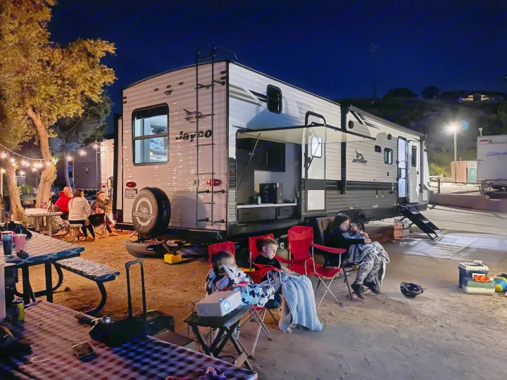 Cozy night at an RV rental campsite: Family & friends relax outdoors, enjoying a movie projected on the travel trailer.. Jayco Jay Flight 2022