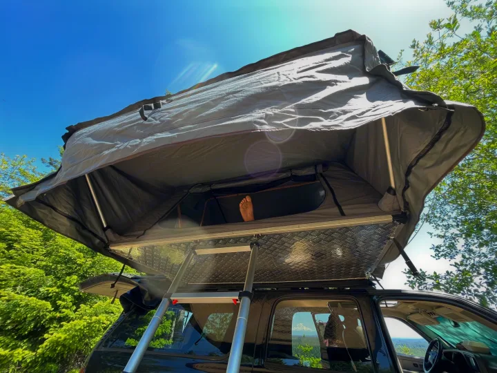 An RV rental alternative: Relax in a rooftop tent on an SUV, foot visible, under blue skies & trees.. Gmc Yukon XL 2005