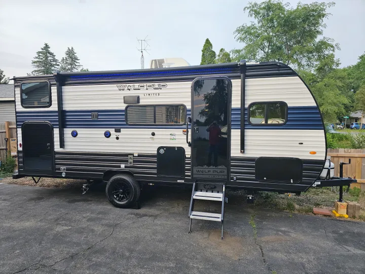A new Wolf Pup travel trailer, ideal for an RV rental, parked on asphalt with steps extended & blue awning lights.. Forest River Wolf pup 17JW 2023